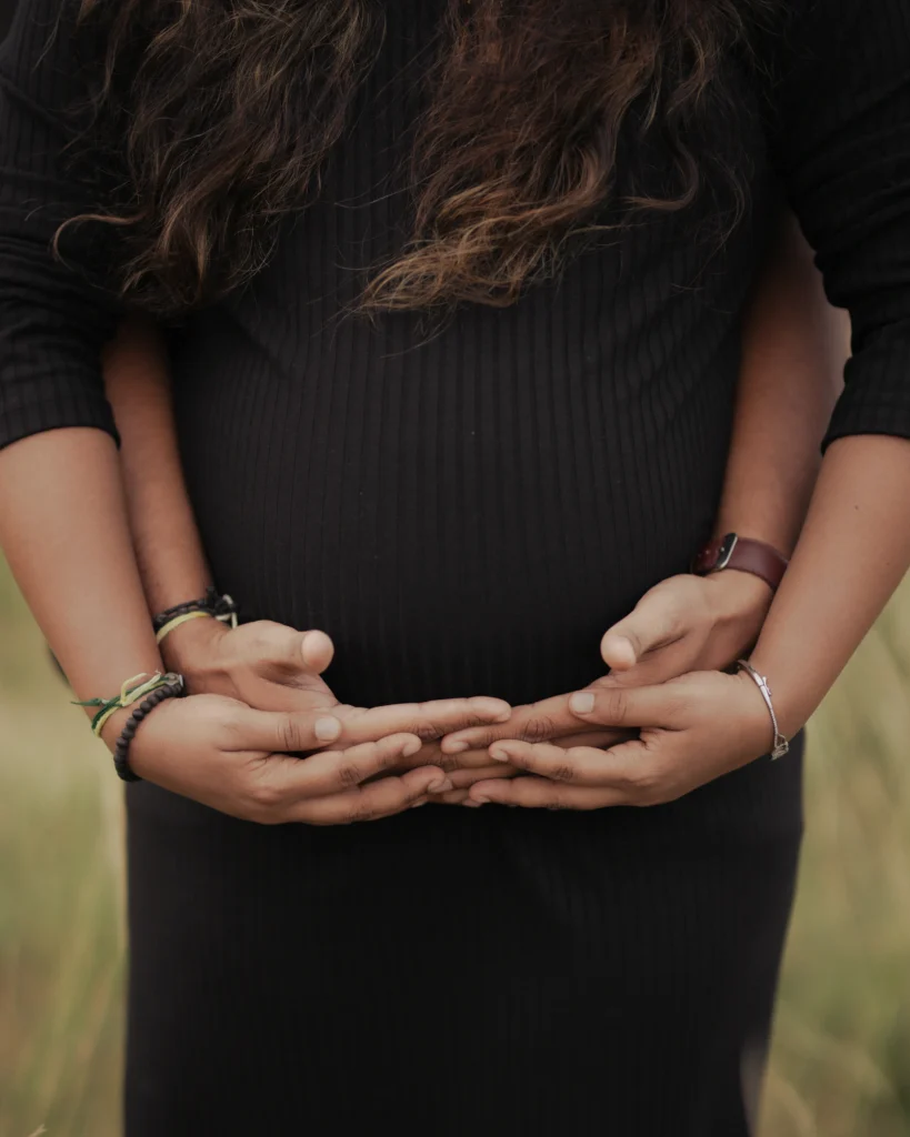 Maternity photoshoot of a pregnant woman in a flowing dress posing outdoors during golden hour.